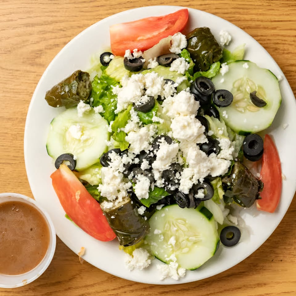 A Marinelli's Pizza Greek salad with lettuce, tomatoes, cucumbers, olives, feta, and stuffed grape leaves.