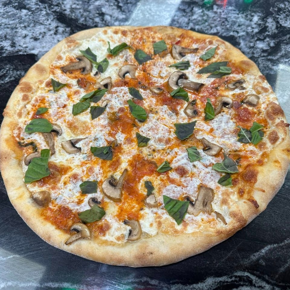 Marinelli's Pizza with mushrooms, basil, white cheese, and red sauce on a dark countertop.